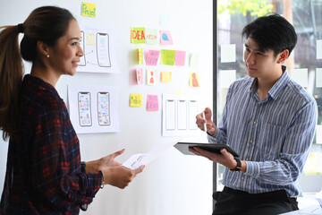 Two website developer presenting and testing mobile app interface design on whiteboard at creative office. © Prathankarnpap