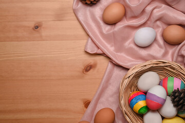 Colorful painted Easter eggs in wicker basket on wooden background with copy space.