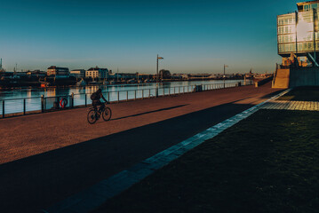 A woman biking on the riverside in Bremen at dawn - obrazy, fototapety, plakaty