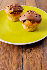 Two chocolate chip muffins on a yellow plate and wooden table . Copy space. Premium quality bakery product.