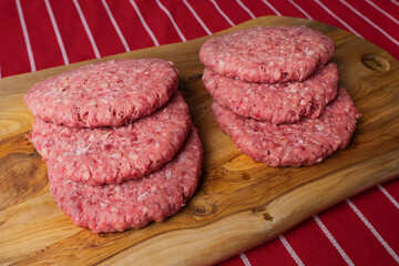 Six simple beef uncooked burgers on a wooden board and red and white butcher apron. Meat industry product. Fast fool meal.