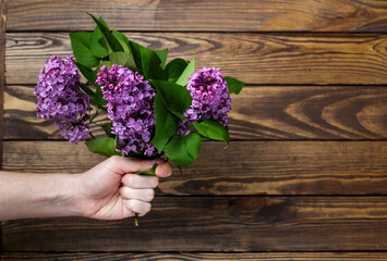 hand holds a bouquet of lilacs on a wooden background