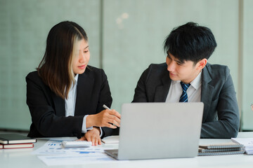 Two young Asian businessmen and women working together meet at the Financial Graphing Computing Office. Share ideas, discuss and train business plans on a laptop.