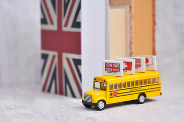 Yellow school bus with the international flags on top and the vintage and english book background for international education concept.