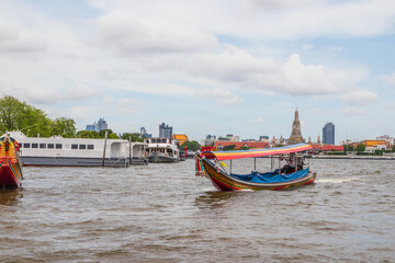 Fototapeta premium A longtail boat, the Chao Phraya River, the Thai royal first class Temple Wat Arun and the Cityscape of Bangkok Thailand Southeast Asia