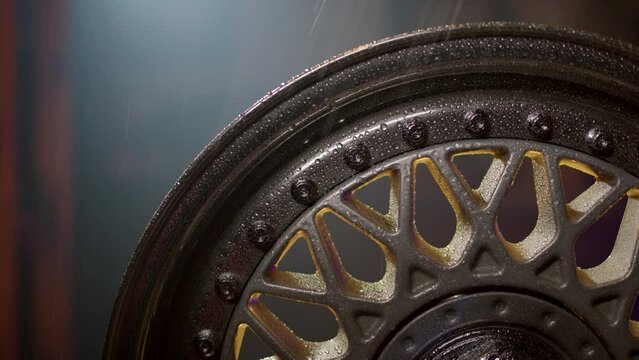 beautiful freshly painted rim from car in rain with water drops on polished shelves and bolts. Classic wheel close up on background of garage in defocus.