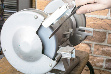 Knife sharpener and hand with blade on table, closeup