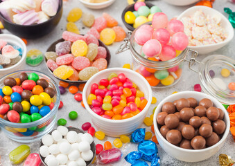 Pink lollipop candies in jar with various milk chocolate and jelly gums candies on white background with liquorice allsorts and strawberry bonbons