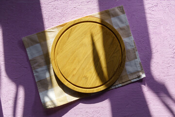 Fototapeta na wymiar Empty wooden round board on the pink kitchen table. Wooden pizza plate, a place to copy. View from above. Mockup