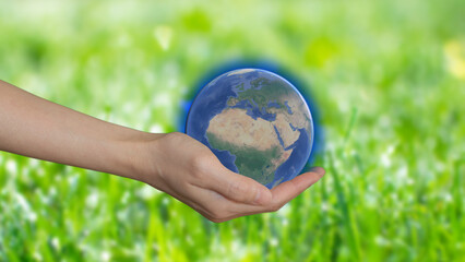 A woman's hand holding model of the planet on green background, earth day concept. Save the green world