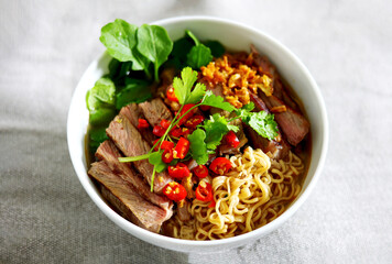 Closeup a bowl of  instant hot Noodles soup with beef added chilli, coriander and baby Broccoli sprouts in white bowl with chopsticks on eating table.