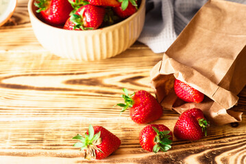 Fresh red strawberries in the bowl and paper bag in the wooden background. Rustic style