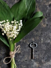 Bouquet of lilies of the valley tied twine and old retro key on black concrete background. Bridal greeting card. Flatlay with spring flowers.
