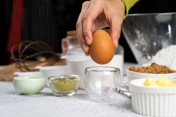 Woman hand in green long sleeve pick up fresh egg from clear glass cup together other ingredient recipes