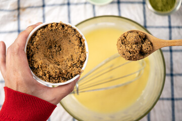Woman hand in red long sleeve pick up brown sugar scoop from bowl over egg flour mixing
