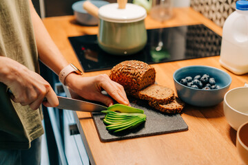 Close-up of a woman's hands slicing a ripe avocado for a sandwich.