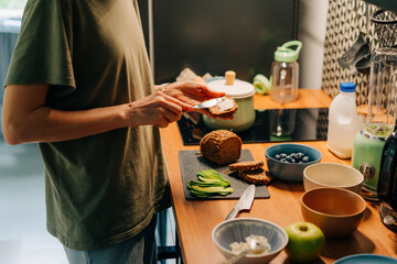 A cropped woman spreads butter or cheese on sandwich bread.