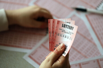 Filling out a lottery ticket. A young woman holds the lottery ticket with complete row of numbers on the lottery blank sheets background.