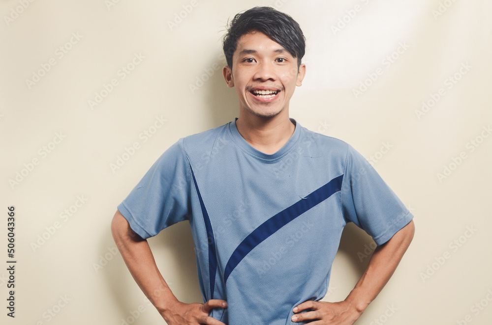 Wall mural Asian young man in sports t-shirt looking happy isolated on background