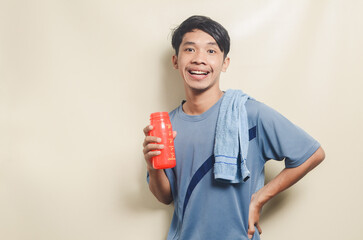 Asian young man in sports t-shirt looking tired and drinking isolated on background