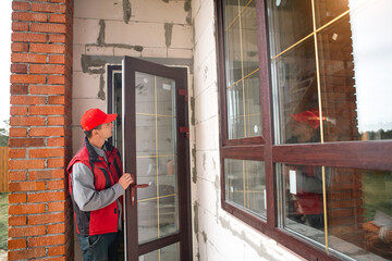 The window installer adjusts the hinges and checks new windows in the cottage under construction....