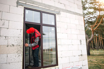 The window installer adjusts the hinges and checks new windows in the cottage under construction....