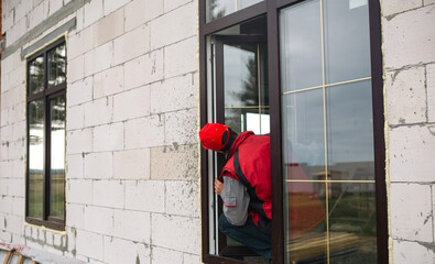 The window installer adjusts the hinges and checks new windows in the cottage under construction....