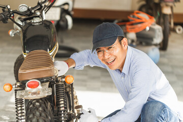 Cheerful mechanic repairing motorcycle in workshop garage, Smiling man fixing motorbike in repair shop, Repairing and maintenance concepts