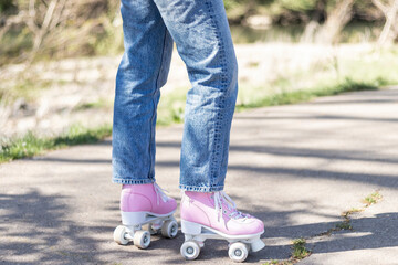 woman's legs in jeans and pink roller skates in a park