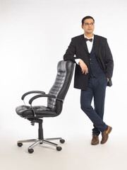 Boss chair. Businessman is standing next to armchair. Man in business suit. Male manager leans on boss chair. Man in suit posing on white background. Concept of selling office furniture.