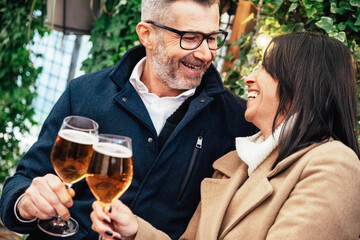 Mature couple having fun drinking beer at cafe bar restaurant - Husband and wife hanging out enjoying happy hour at brewery pub - obrazy, fototapety, plakaty