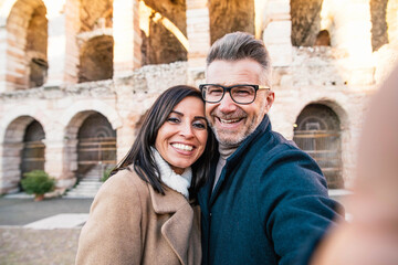 Fototapeta na wymiar Married couple visiting Colosseum, Rome - Happy tourists visiting Italian famous place - Husband and wife taking selfie picture hanging in a romantic date outside - Tourism lifestyle concept