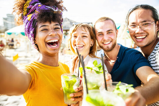 Multiracial friends cheering cocktails at beach party - Young people laughing together having fun on summer vacation - Friendship concept with guys and girls smiling outside on summertime holiday