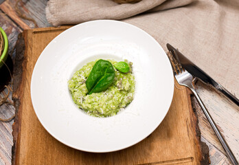 Plate serving of green risotto with basil leaves and cheese. Healthy food. Tender arborio flavored with spinach greens and infused with lamb meat broth