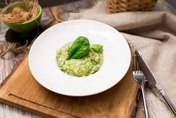 Plate serving of green risotto with basil leaves and cheese. Healthy food. Tender arborio flavored with spinach greens and infused with lamb meat broth