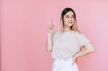 Portrait of a woman points with her index finger to a free space on the background and looks to side