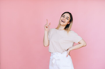 Portrait of a woman points her index finger at a free space on the background and smiles broadly