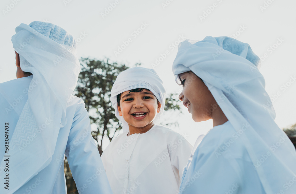 Wall mural children playing together in dubai in the park. group of kids wearing traditional kandura white dres