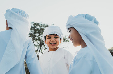 Children playing together in Dubai in the park. Group of kids wearing traditional kandura white...