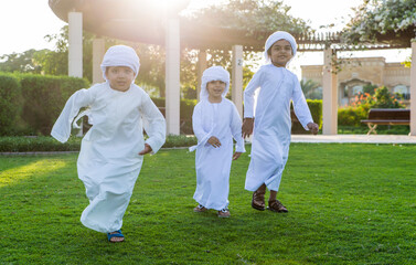 Children playing together in Dubai in the park. Group of kids wearing traditional kandura white...