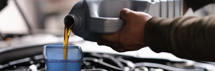 A man pours oil into the car from a canister