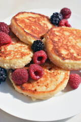 Cottage cheese pancakes, homemade syrniki, curd fritters with raspberry and blackberry on white plate, close up food, vertical image