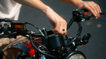 young man's hands hold motorbike steering wheel as he touches brake lever turning ignition key