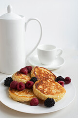 Cottage cheese pancakes, homemade syrniki, curd fritters with raspberry and blackberry on white plate, served with coffee cup