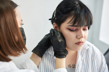 A beautician makes a puncture of the earlobe with a disposable device in a beauty salon. Ear...