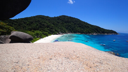 The guy is sitting on a rock and looking at the lagoon. A heavenly place on Earth - turquoise water, white sand, high rocks covered with trees. A place to relax. There are speedboats in the distance