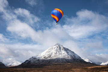 Digital composite image of hot air balloons flying over Beautiful iconic landscape Winter image of Stob Dearg Buachaille Etive Mor mountain in Scottish Highlands againstd vibrant blue sky