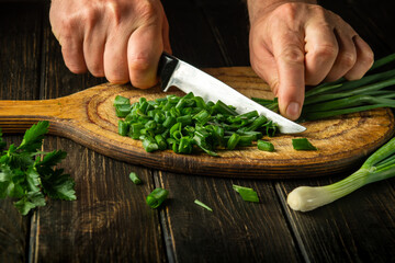 Cook cutting green onion on a cutting board with a knife for preparing a vegetarian dish. Peasant food.