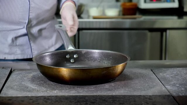 Male chef pours sunflower oil from bottle into hot empty frying pan in restaurant's kitchen. Cooking, frying in the kitchen. Dolly sloping video.