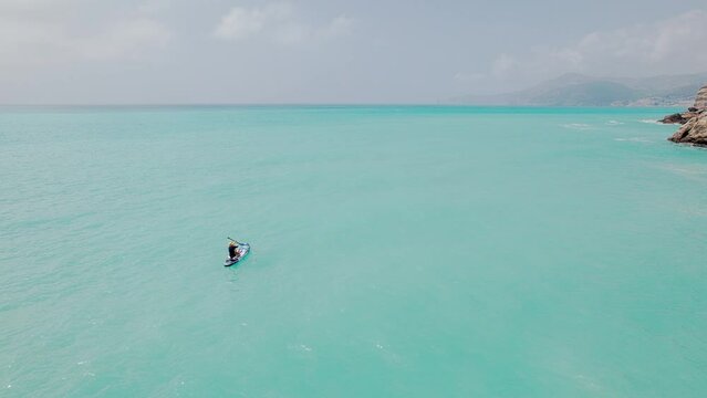 Young woman and kid oaring on a stand up paddle board. Mom and son surfing down azure sea on supboard. Aerial view